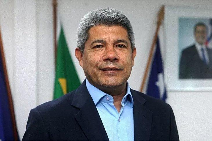Jerônimo Rodrigues, candidato ao governo da Bahia pelo PT. Ele tem cabelo liso, curto e grisalho. Ele sorri para a câmera em sala fechada, com bandeiras atrás - Metrópoles