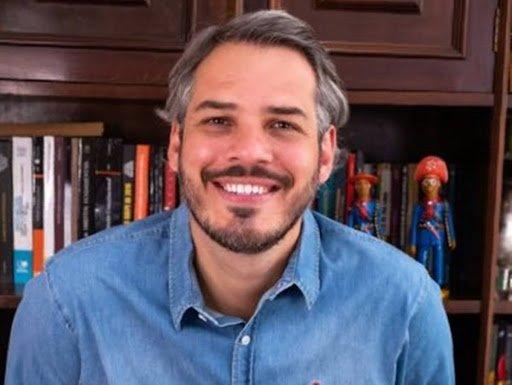 Tiago Botelho, candidato a senador do Mato Grosso do Sul pelo PT. Ele é branco, tem cabelo grisalho, ondulado e médio e sorri para a foto, frente a uma estante de livros - Metrópoles